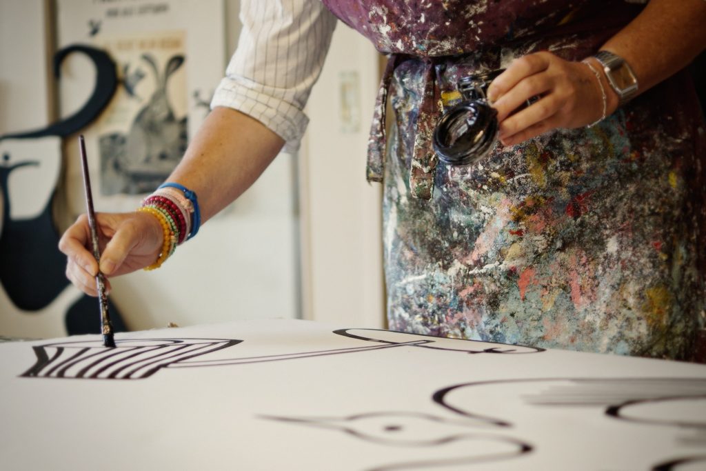 Maker schildert met penseel en inkt zwarte lijnen op een groot wit paneel in het atelier
